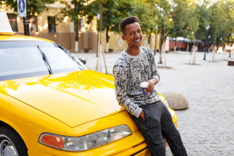 Homem novo de sorriso com caf? do copo o ? disposi??o e onever no bolso, assentado na capa fotografia de stock Homem novo de sorriso com caf? do copo o ? disposi??o e onever no bolso, assentado na capa fotografia de stock