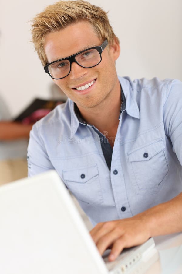 Homem novo de sorriso que trabalha no escritório imagem de stock Homem novo de sorriso que trabalha no escritório imagem de stock