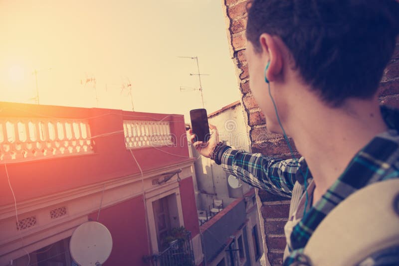 Homem novo do viajante que faz a foto com telefone celular no telhado imagem de stock Homem novo do viajante que faz a foto com telefone celular no telhado imagem de stock