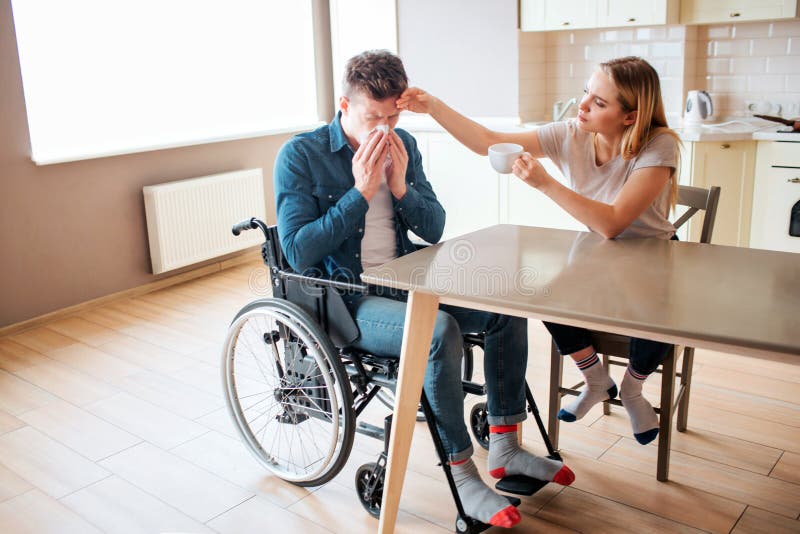 Homem novo doente com necessidades e espirrar especiais da inabilidade Indiv?duo doente e doente A jovem mulher senta-se ao lado imagem de stock royalty free Homem novo doente com necessidades e espirrar especiais da inabilidade Indiv?duo doente e doente A jovem mulher senta-se ao lado imagem de stock royalty free