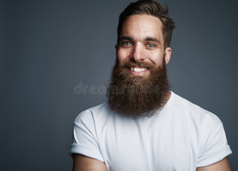 Homem novo farpado que sorri contra um fundo cinzento fotografia de stock Homem novo farpado que sorri contra um fundo cinzento fotografia de stock