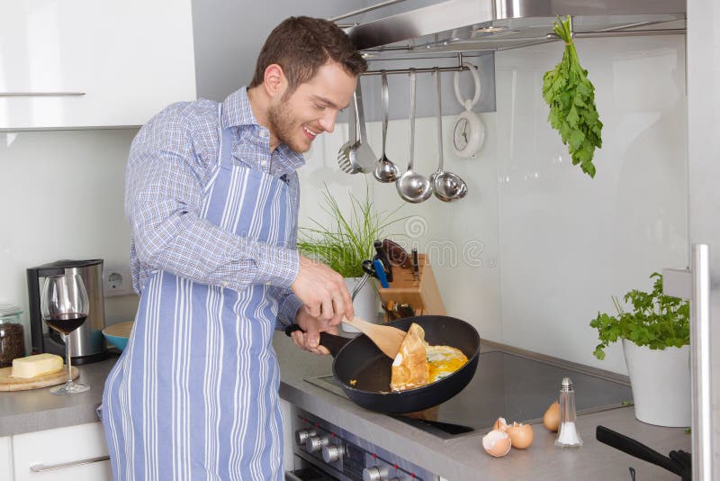 Homem novo na cozinha que cozinha ovos fritos fotografia de stock Homem novo na cozinha que cozinha ovos fritos fotografia de stock