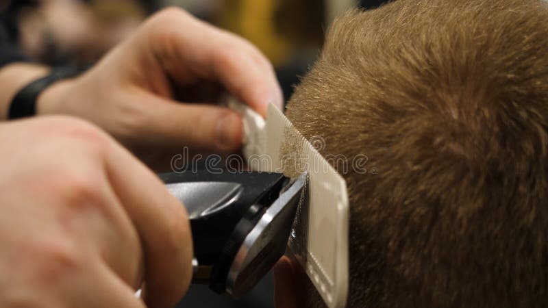 Homem novo no conceito de Barber Shop Hair Care Service Equipe as mãos do ` s que fazem um corte de cabelo para o homem na barbea imagem de stock royalty free Homem novo no conceito de Barber Shop Hair Care Service Equipe as mãos do ` s que fazem um corte de cabelo para o homem na barbea imagem de stock royalty free