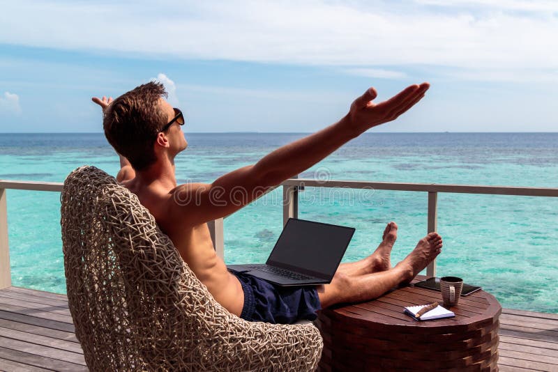 Homem novo no funcionamento do roupa de banho em um port?til em um destino tropical os braços aumentaram, conceito da liberdade foto de stock royalty free Homem novo no funcionamento do roupa de banho em um port?til em um destino tropical os braços aumentaram, conceito da liberdade foto de stock royalty free