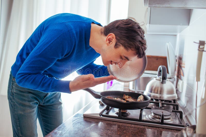 Homem novo que aspira o alimento da bandeja na cozinha imagens de stock royalty free Homem novo que aspira o alimento da bandeja na cozinha imagens de stock royalty free