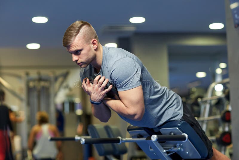 Homem novo que dobra os músculos traseiros no banco no gym imagem de stock royalty free Homem novo que dobra os músculos traseiros no banco no gym imagem de stock royalty free