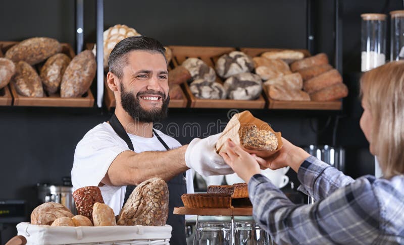 Homem novo que dá o pão fresco à mulher na padaria