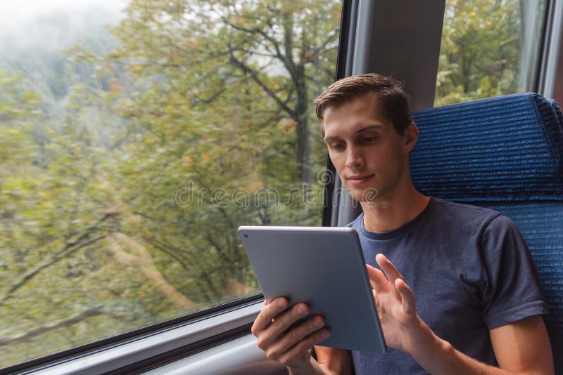 Homem novo que estuda com uma tabuleta ao viajar pelo trem fotografia de stock Homem novo que estuda com uma tabuleta ao viajar pelo trem fotografia de stock
