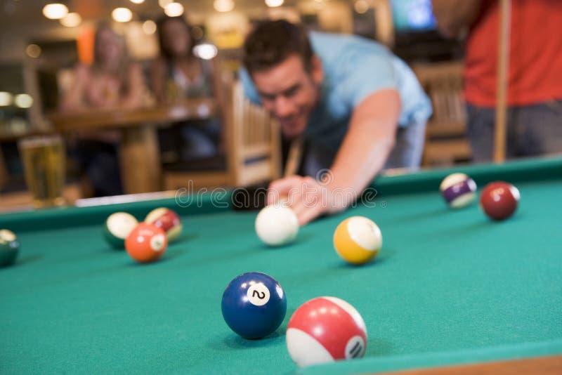 Young man playing pool in a bar (focus on pool table). Young man playing pool in a bar (focus on pool table)