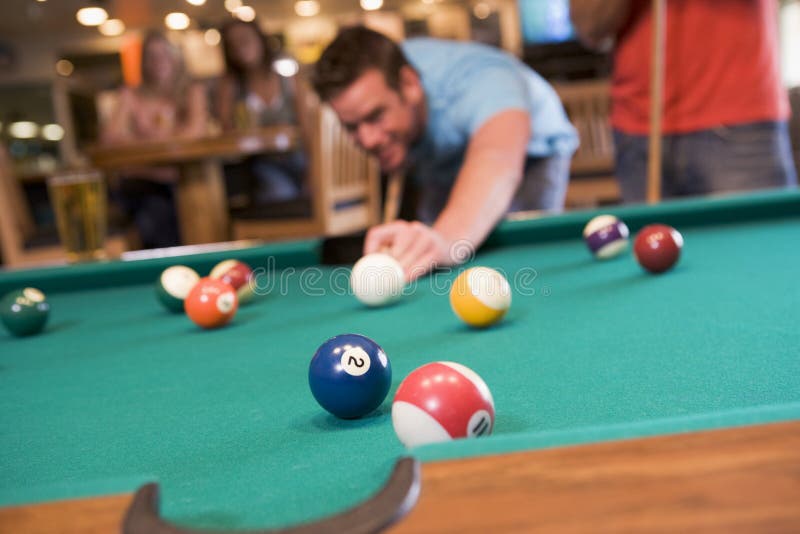 Young man playing pool in a bar, focus on the pool table. Young man playing pool in a bar, focus on the pool table