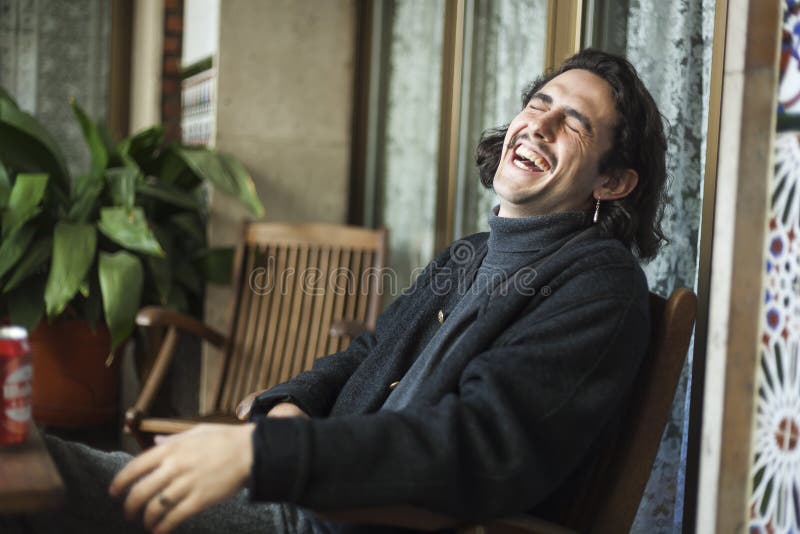 Homem novo que ri duramente em um terraço fotografia de stock Homem novo que ri duramente em um terraço fotografia de stock