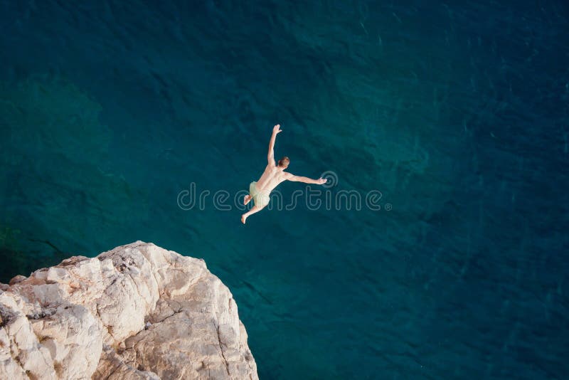 Homem novo que salta do penhasco no mar imagem de stock royalty free Homem novo que salta do penhasco no mar imagem de stock royalty free