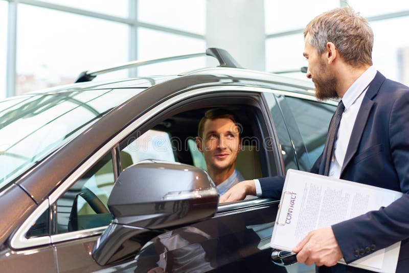 Homem novo que testa o carro novo na sala de exposições foto de stock Homem novo que testa o carro novo na sala de exposições foto de stock