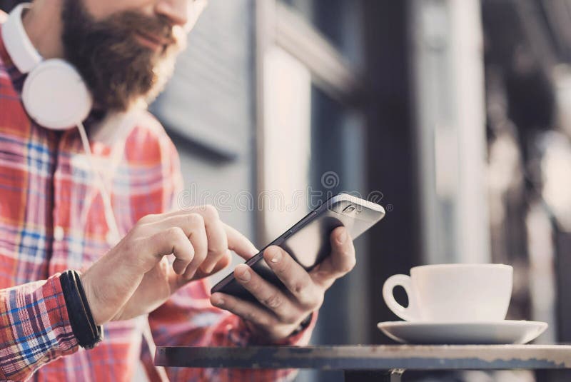 Homem novo que texting em seu smartphone na cidade Feche acima do adulto alegre usando o telefone celular em um café