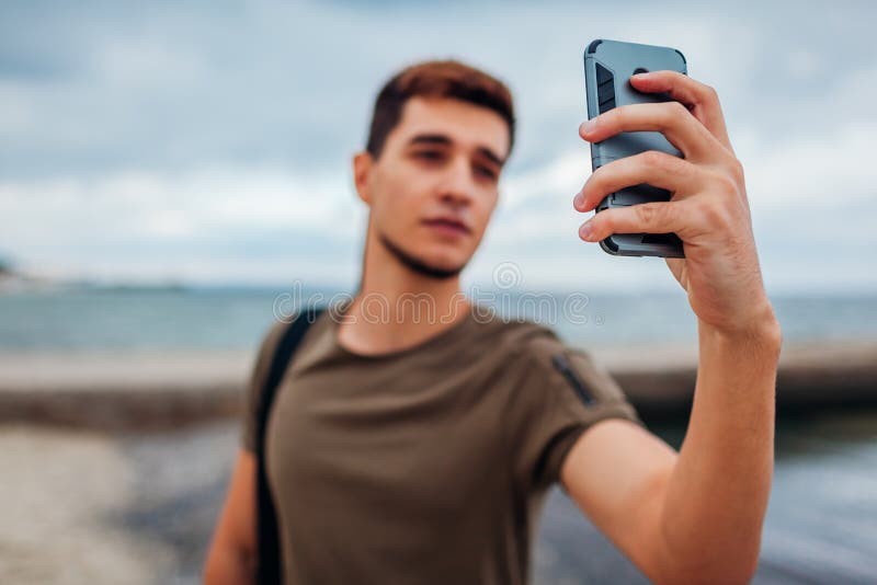 Homem novo que toma o selfie usando o telefone na praia nebulosa Indivíduo desportivo considerável que anda pelo cais fotos de stock Homem novo que toma o selfie usando o telefone na praia nebulosa Indivíduo desportivo considerável que anda pelo cais fotos de stock