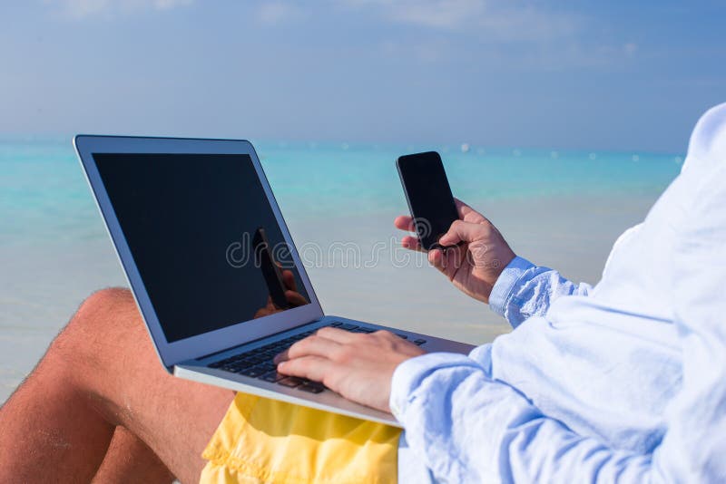 Homem novo que trabalha no portátil na praia tropical imagem de stock royalty free Homem novo que trabalha no portátil na praia tropical imagem de stock royalty free