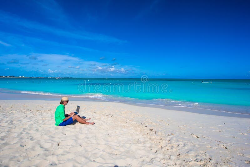 Homem novo que usa o portátil na praia tropical foto de stock Homem novo que usa o portátil na praia tropical foto de stock