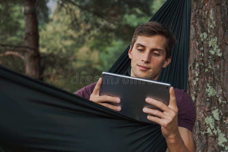 Homem novo que usa uma tabuleta em uma rede imagem de stock Homem novo que usa uma tabuleta em uma rede imagem de stock