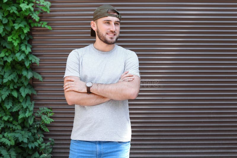 Homem novo que veste o t-shirt cinzento perto da parede imagens de stock Homem novo que veste o t-shirt cinzento perto da parede imagens de stock
