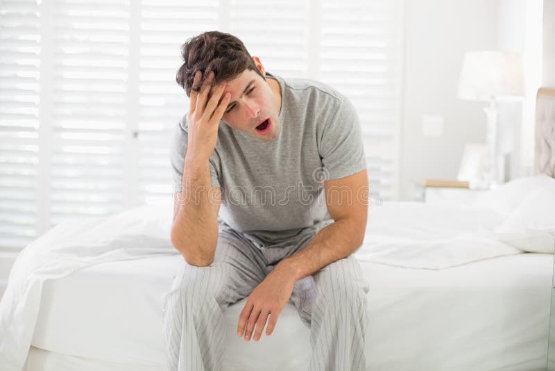 Homem novo sonolento que senta-se e que boceja na cama fotos de stock Homem novo sonolento que senta-se e que boceja na cama fotos de stock