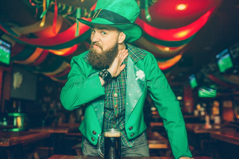 Homem novo sério e louco no suporte do terno de St Patrick no bar e no olhar na câmera Guarda a mão perto do pescoço Agressivo fotos de stock Homem novo sério e louco no suporte do terno de St Patrick no bar e no olhar na câmera Guarda a mão perto do pescoço Agressivo fotos de stock