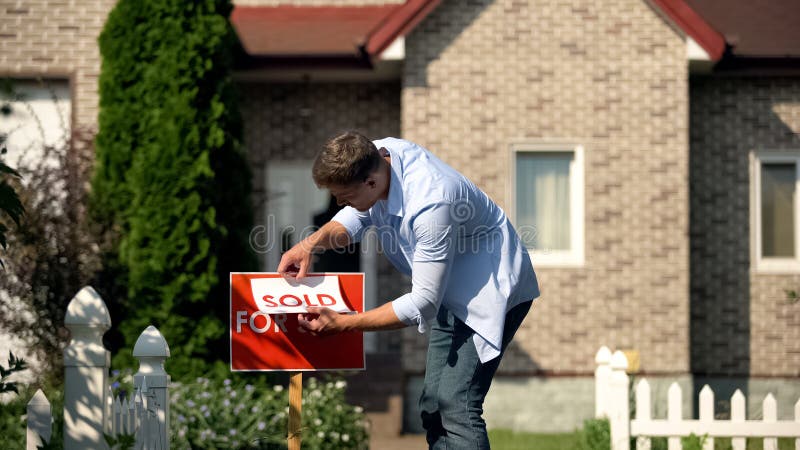 Homem orgulhoso mudando para venda para placa vendida na frente da casa, comprar nova casa foto de stock royalty free Homem orgulhoso mudando para venda para placa vendida na frente da casa, comprar nova casa foto de stock royalty free