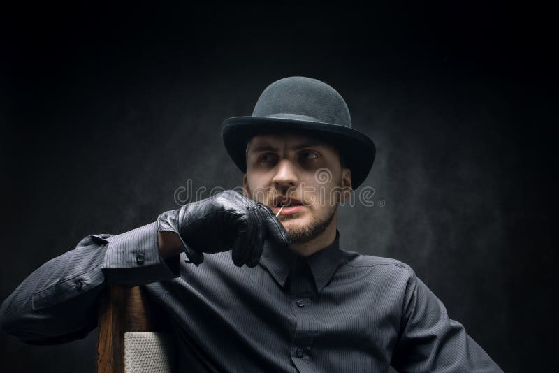 Homem pensativo em um chapéu e palito em sua boca, contra um fundo escuro fotos de stock royalty free Homem pensativo em um chapéu e palito em sua boca, contra um fundo escuro fotos de stock royalty free