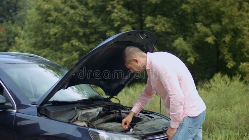 Homem preocupado que olha sob a capa do carro em exterior