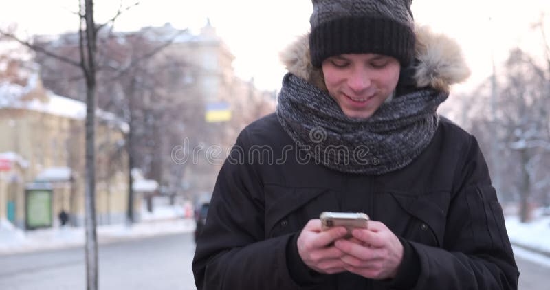 Homem que anda e que usa o telefone celular em um dia de inverno frio