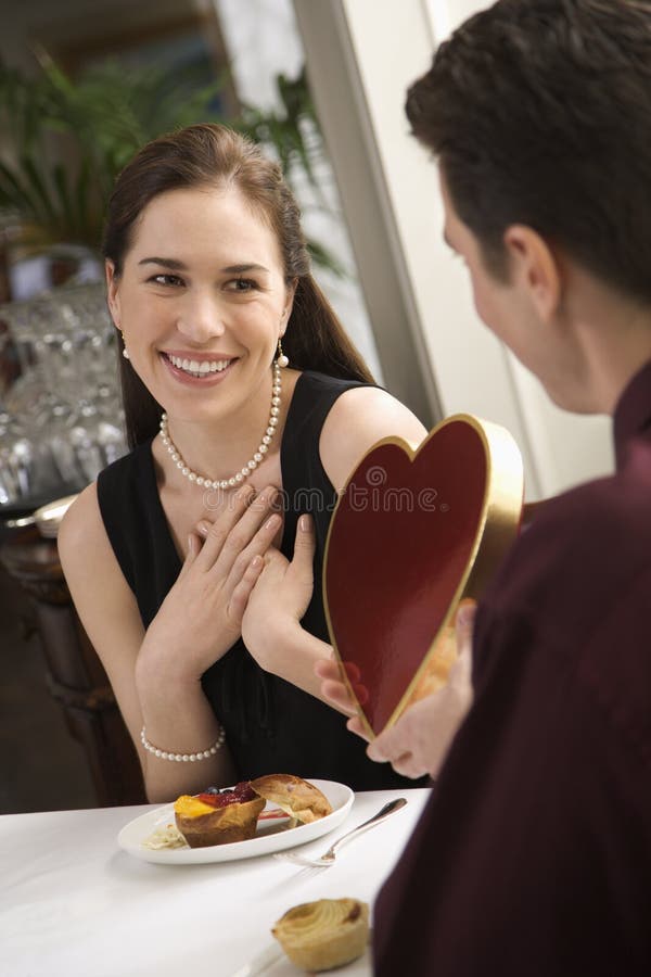 Mid adult Caucasian man giving a heart shaped box of chocolates to woman at restaurant. Mid adult Caucasian man giving a heart shaped box of chocolates to woman at restaurant.