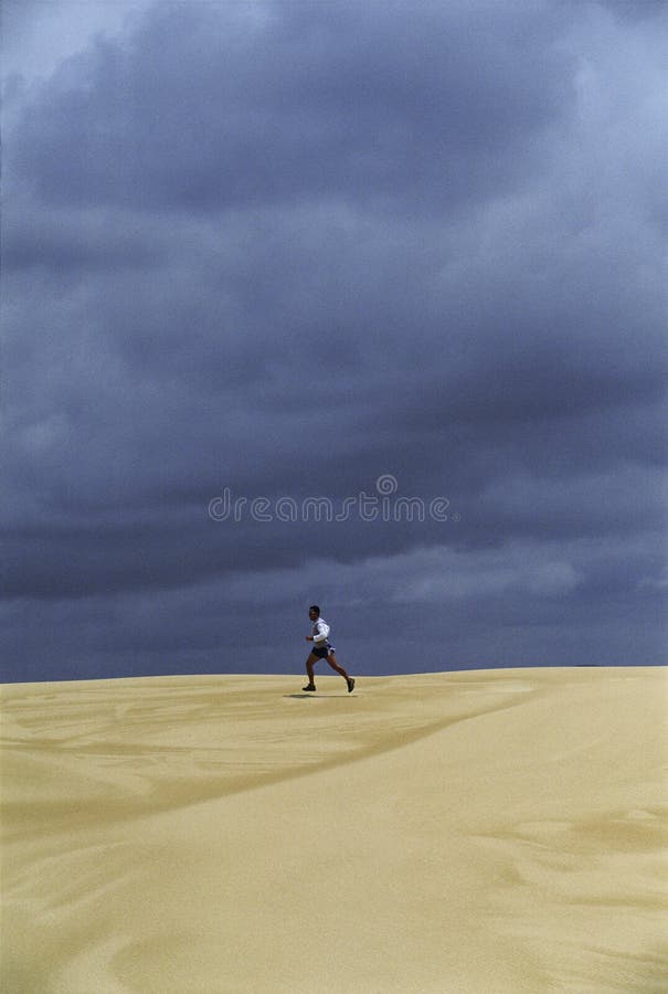Homem que funciona através dos planos da areia imagem de stock royalty free Homem que funciona através dos planos da areia imagem de stock royalty free