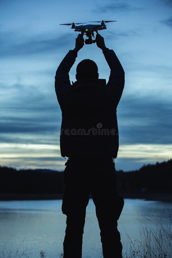 Homem que guarda um zangão para a fotografia aérea Silhueta contra t imagem de stock royalty free Homem que guarda um zangão para a fotografia aérea Silhueta contra t imagem de stock royalty free