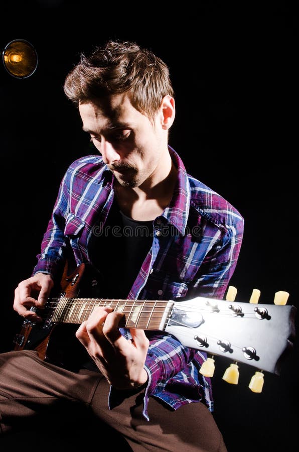 Homem que joga a guitarra na sala escura foto de stock Homem que joga a guitarra na sala escura foto de stock