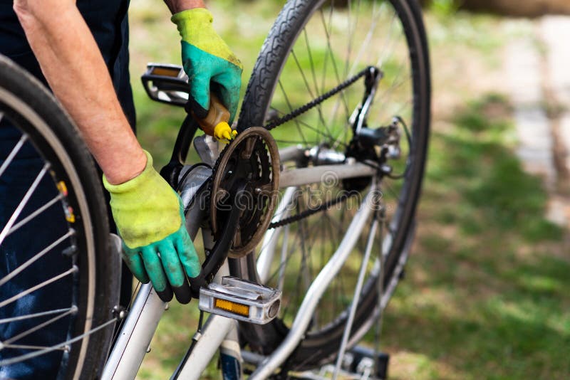 Homem que lubrifica a corrente da bicicleta que mantém para a estação nova imagem de stock royalty free Homem que lubrifica a corrente da bicicleta que mantém para a estação nova imagem de stock royalty free