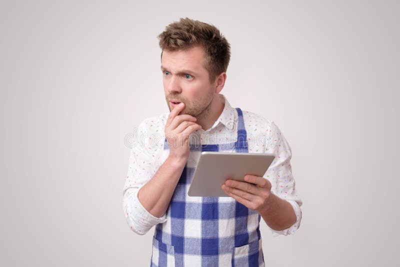 Homem que olha a receita na tabuleta digital para preparar o bolo imagens de stock royalty free Homem que olha a receita na tabuleta digital para preparar o bolo imagens de stock royalty free