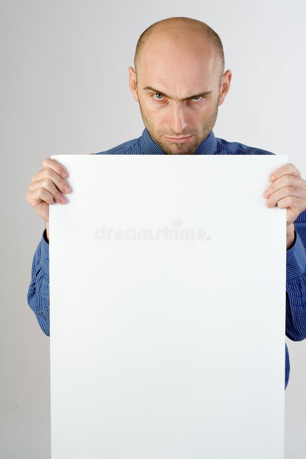 A portrait of a adult man in a blue dress shirt holding a blank white sign on a white background. He has a serious expression on hes face and one of his eyebrows is raised. A portrait of a adult man in a blue dress shirt holding a blank white sign on a white background. He has a serious expression on hes face and one of his eyebrows is raised.