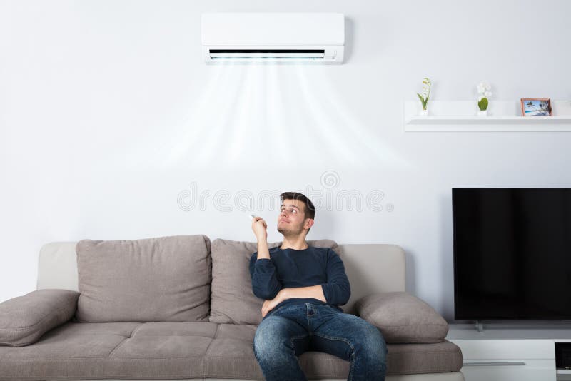 Homem que senta-se no condicionador de ar de funcionamento do sofá