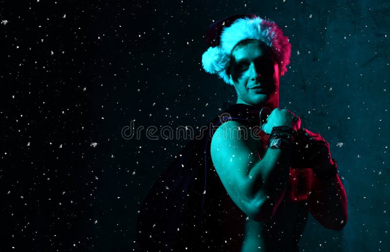 Homem 'sexy' no traje de Santa Claus Christmas com saco completamente dos presentes sob confetes da neve imagens de stock royalty free Homem 'sexy' no traje de Santa Claus Christmas com saco completamente dos presentes sob confetes da neve imagens de stock royalty free