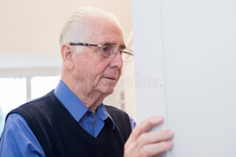 Homem superior esquecido com a demência que olha no armário em casa imagens de stock Homem superior esquecido com a demência que olha no armário em casa imagens de stock