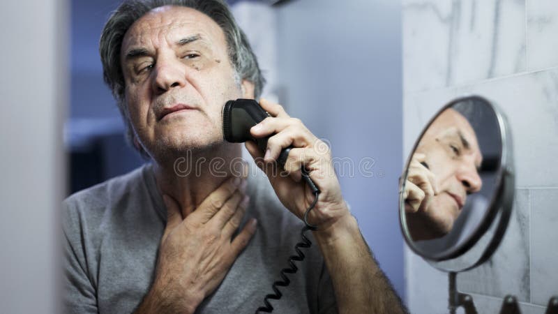 Homem superior que barbeia sua barba no banheiro imagem de stock royalty free Homem superior que barbeia sua barba no banheiro imagem de stock royalty free