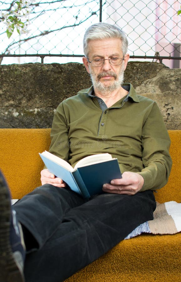 Homem superior que lê um livro no sofá-cama fora foto de stock Homem superior que lê um livro no sofá-cama fora foto de stock