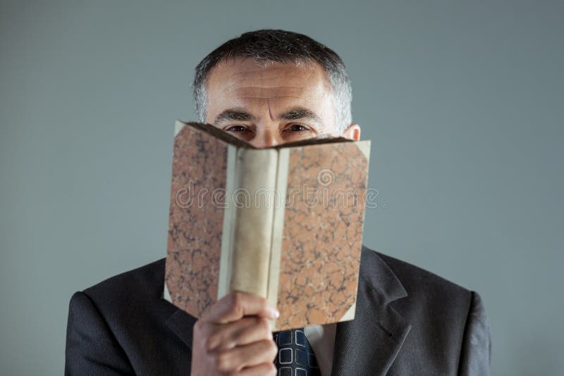 Homem superior que olha a câmera atrás de um livro velho imagem de stock Homem superior que olha a câmera atrás de um livro velho imagem de stock