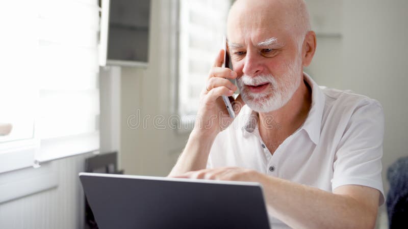 Homem superior que senta-se em casa com portátil e smartphone Usando o telefone celular que discute o projeto na tela foto de stock Homem superior que senta-se em casa com portátil e smartphone Usando o telefone celular que discute o projeto na tela foto de stock