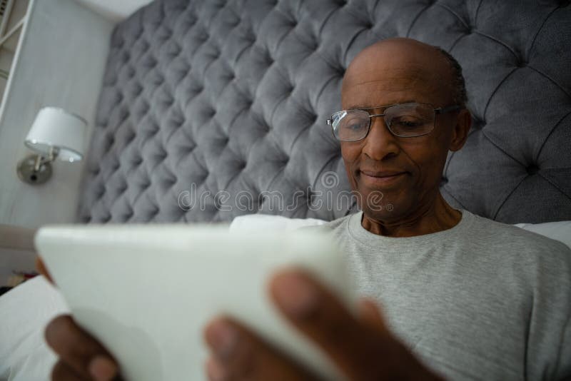 Homem superior que usa a tabuleta digital ao relaxar na cama fotografia de stock Homem superior que usa a tabuleta digital ao relaxar na cama fotografia de stock