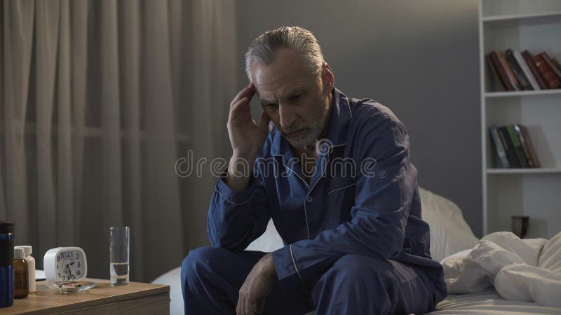 Homem superior sem sono que sofre da dor de cabeça, sentando-se no sofá na noite imagem de stock royalty free Homem superior sem sono que sofre da dor de cabeça, sentando-se no sofá na noite imagem de stock royalty free