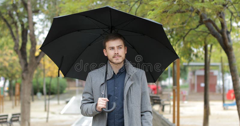 Homem sério que anda sob a chuva no inverno