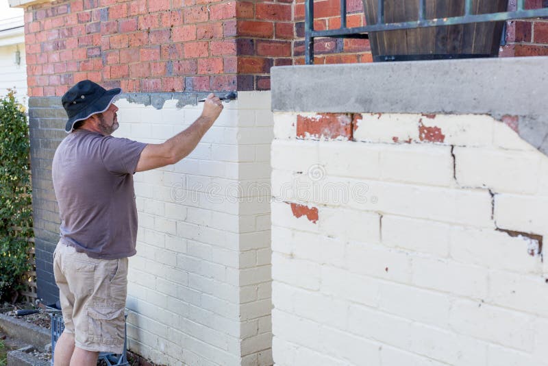 Homem sênior pintando o exterior de uma casa suburbana de tijolos foto de stock Homem sênior pintando o exterior de uma casa suburbana de tijolos foto de stock