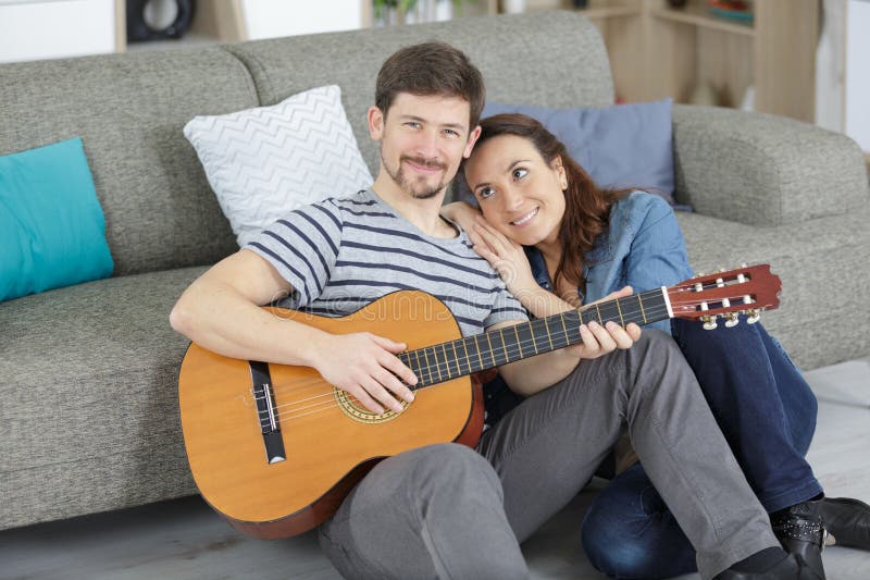Homem tocando violão acústico no sofá para mulher fotos de stock royalty free