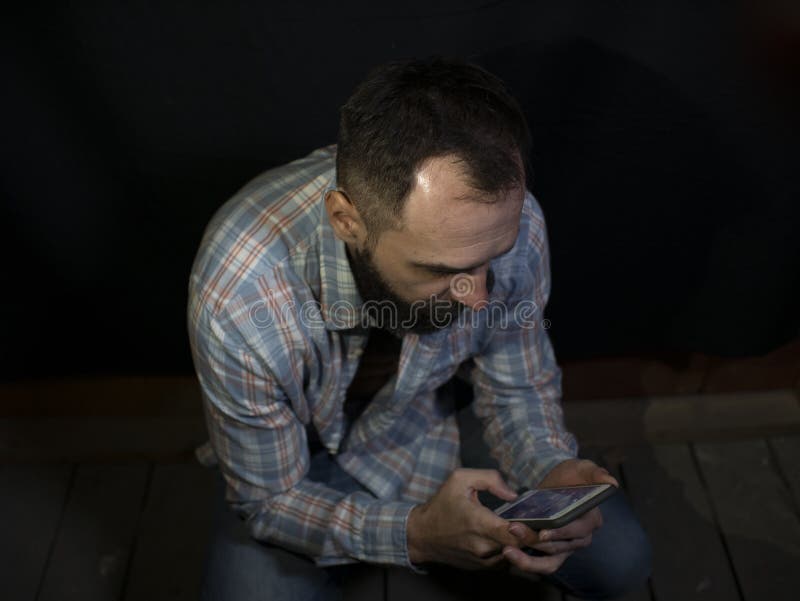 Homem à moda com uma barba e olhares squatting do bigode na tela do telefone celular imagens de stock Homem à moda com uma barba e olhares squatting do bigode na tela do telefone celular imagens de stock