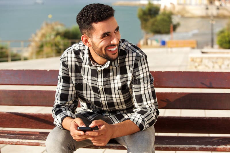 Homem árabe novo que sorri fora com telefone celular imagens de stock royalty free Homem árabe novo que sorri fora com telefone celular imagens de stock royalty free